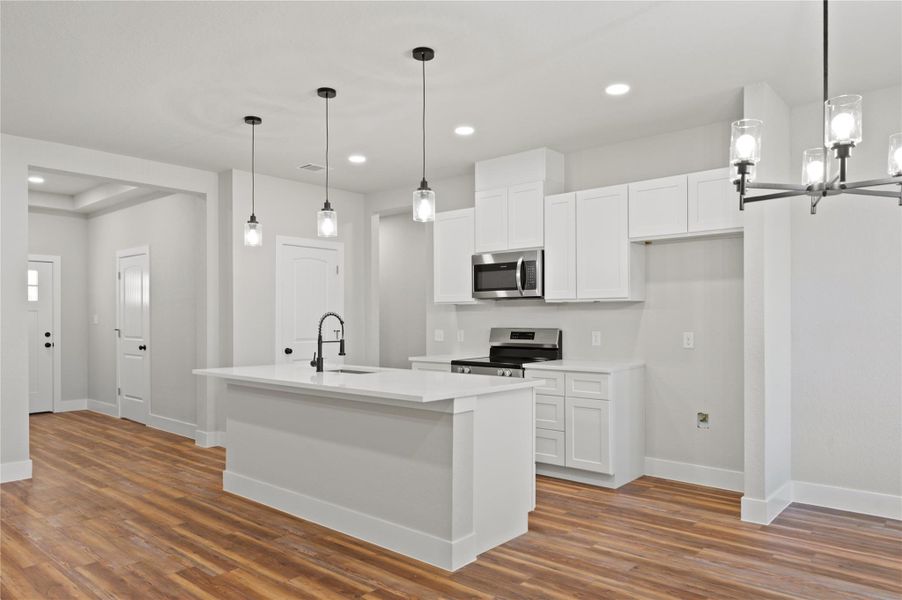 Kitchen featuring stainless steel appliances, an island with sink, white cabinetry, dark wood-type flooring, and hanging lights