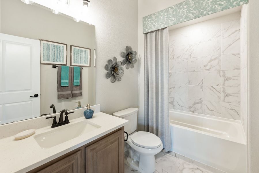 Full bathroom with wood vanity, white countertop, and tub-shower combo with marble tile surround