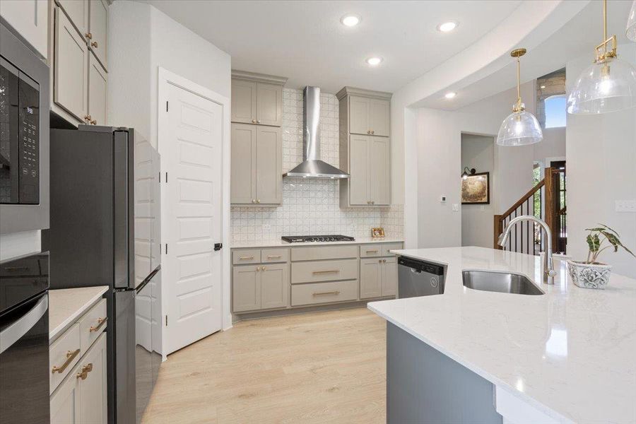 Kitchen with gray cabinetry, stainless steel appliances, light wood-style flooring, light stone counters, and tasteful backsplash