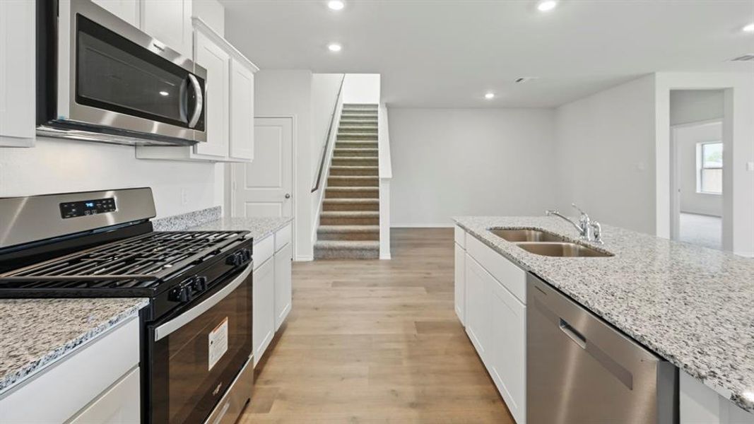 Kitchen with appliances with stainless steel finishes, white cabinetry, light stone countertops, recessed lighting, and light wood-type flooring