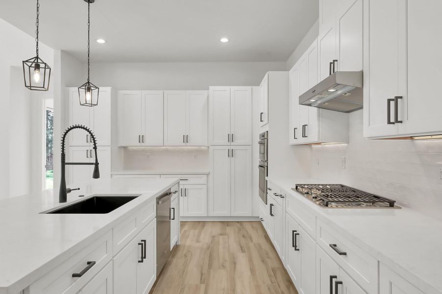Bright, modern chef’s kitchen featuring quartz countertops, custom shaker cabinetry, designer lighting, and a large island with farmhouse sink and pull-down faucet. Stainless steel appliances and under-cabinet lighting complete the clean contemporary design.