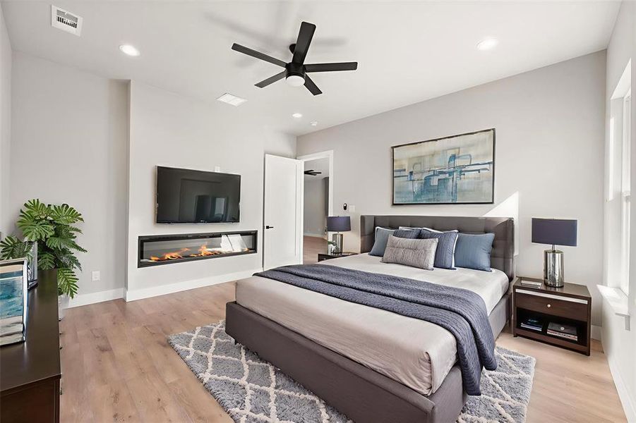 Bedroom with a glass covered fireplace, light wood-style floors, ceiling fan, and recessed lighting Bedroom with a glass covered fireplace, light wood-style floors, ceiling fan, and recessed lighting