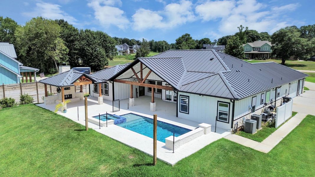 Modern ranch-style home with sleek metal roof, featuring a spacious patio and inviting pool area, perfect for outdoor entertaining. Modern ranch-style home with sleek metal roof, featuring a spacious patio and inviting pool area, perfect for outdoor entertaining.