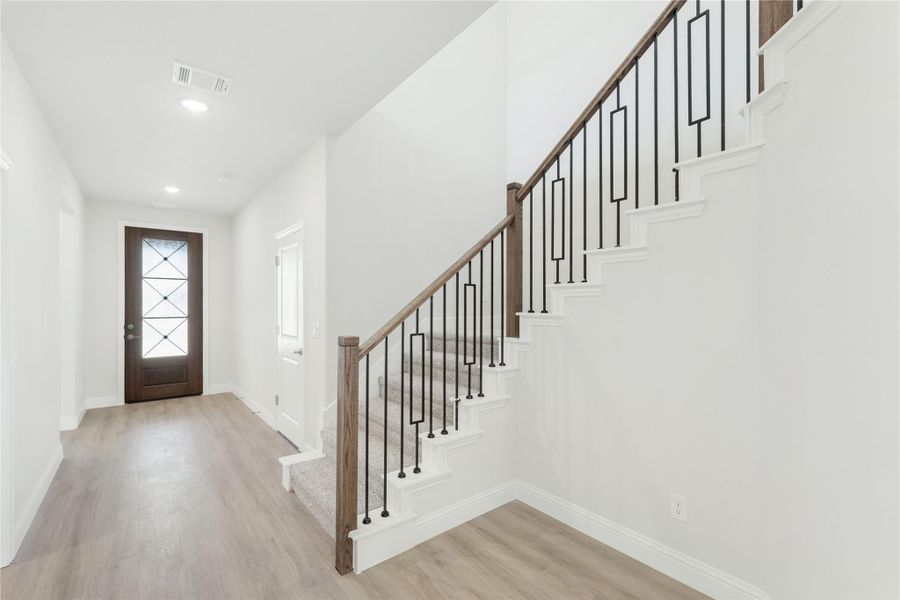Entryway with wood and iron staircase railing, hardwood floors, and glass-panel front door