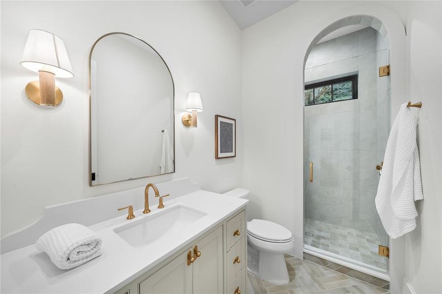 Contemporary bathroom featuring an arched frameless mirror, brass-finish fixtures, and a white vanity with integrated sink