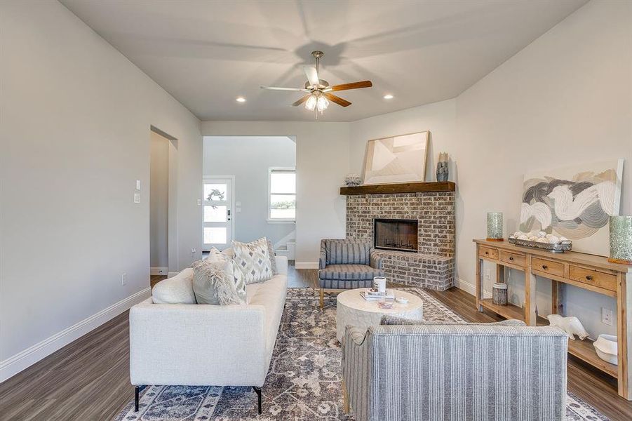 Living room featuring dark wood finished floors, a brick fireplace, recessed lighting, and a ceiling fan
