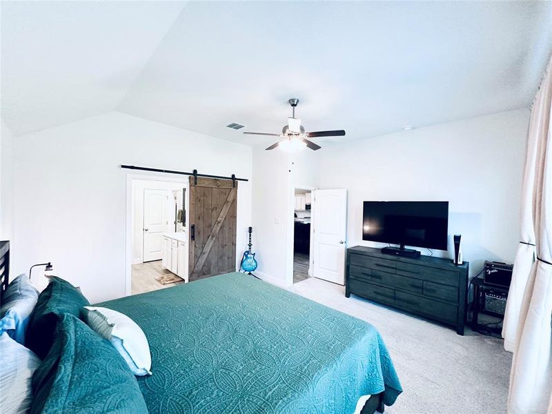 Bedroom with connected bathroom, ceiling fan, light carpet, a barn door, and lofted ceiling