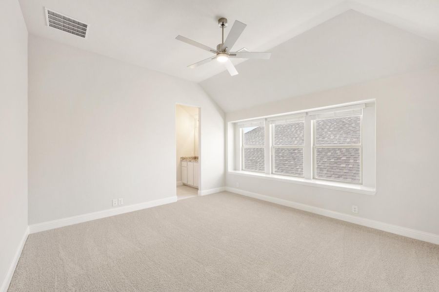 Empty bedroom with vaulted ceiling, ceiling fan, carpet flooring, and ensuite bathroom doorway