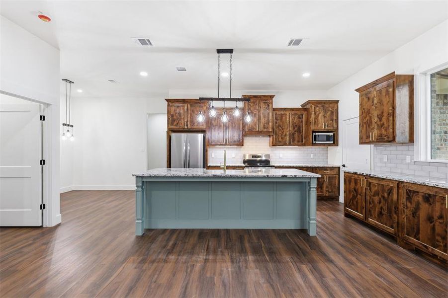 Spacious kitchen featuring a large island with a light blue base and a light-toned countertop, contrasting with warm wood-finish cabinetry Spacious kitchen featuring a large island with a light blue base and a light-toned countertop, contrasting with warm wood-finish cabinetry