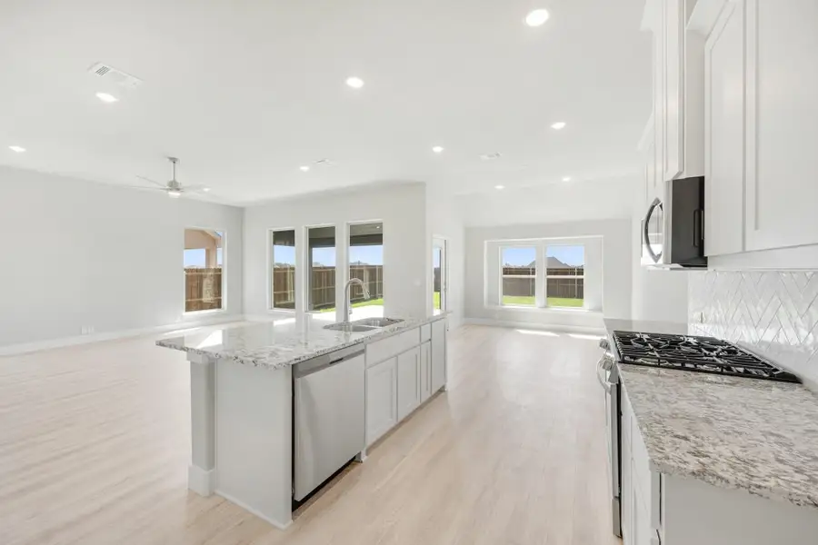 Open kitchen with white cabinets, granite island, and stainless appliances flowing into a bright living area with hardwood floors