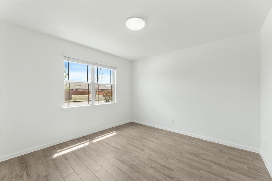 Empty bedroom with white walls, wood-look tile floors, and a large window with natural light