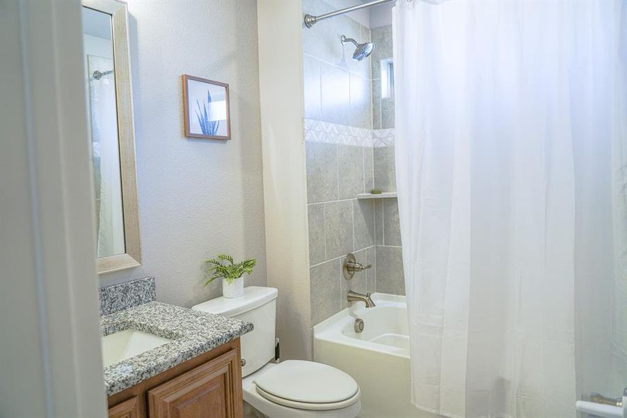Bathroom with shower / bathtub combination with curtain, vanity, and a textured wall