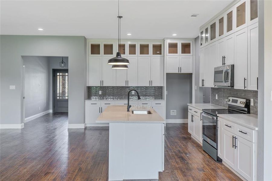 Kitchen with stainless steel appliances, pendant lighting, a center island with sink, tasteful backsplash, and light stone countertops Kitchen with stainless steel appliances, pendant lighting, a center island with sink, tasteful backsplash, and light stone countertops