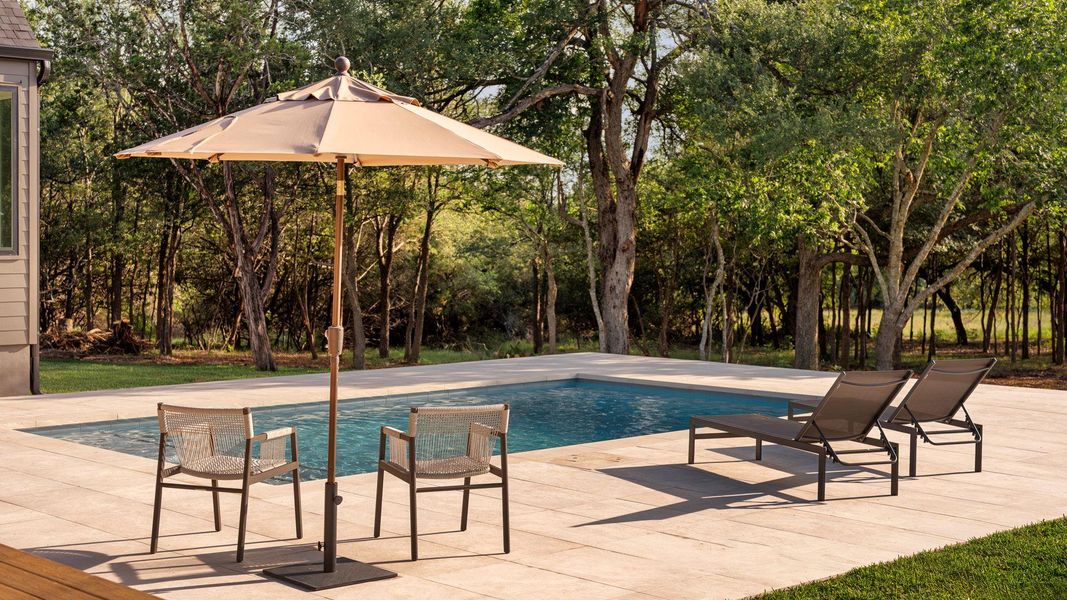 An inviting backyard oasis offers a sparkling in-ground pool and ample space for poolside lounging with a view of nature An inviting backyard oasis offers a sparkling in-ground pool and ample space for poolside lounging with a view of nature