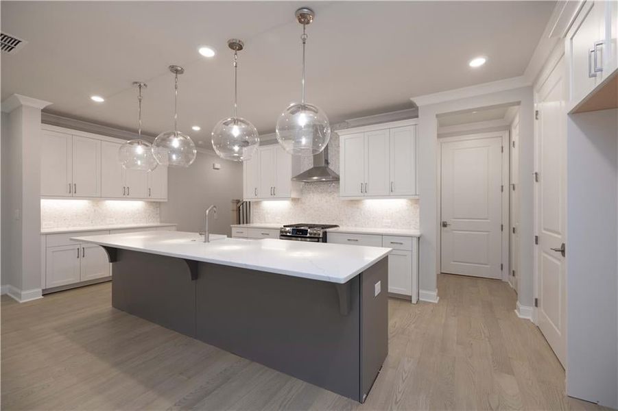 Kitchen featuring hanging light fixtures, stainless steel range with gas stovetop, white cabinets, and a center island with sink