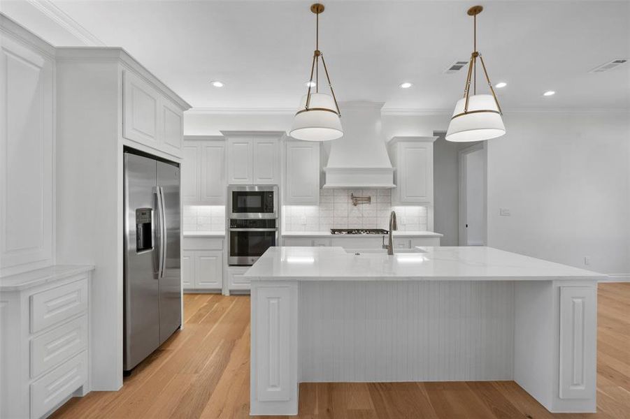 Kitchen with appliances with stainless steel finishes, premium range hood, light hardwood / wood-style flooring, white cabinetry, and hanging light fixtures