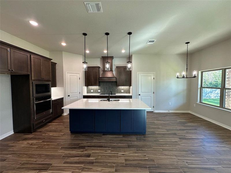 Kitchen with dark brown cabinets, hanging light fixtures, an island with sink, appliances with stainless steel finishes, and dark wood finished floors Kitchen with dark brown cabinets, hanging light fixtures, an island with sink, appliances with stainless steel finishes, and dark wood finished floors