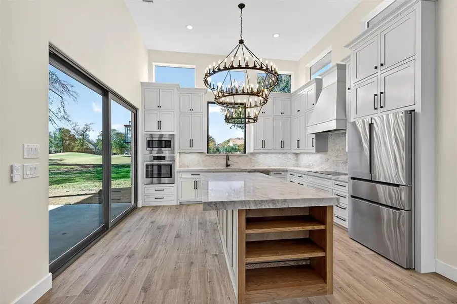 Kitchen featuring open shelves, stainless steel appliances, custom range hood, light stone countertops, and a center island