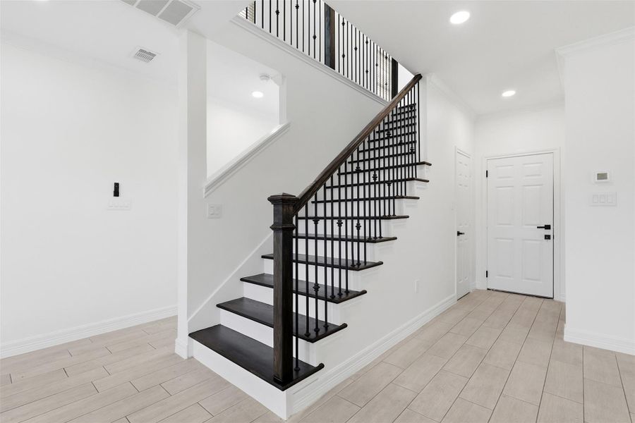 Elegant staircase with sleek black iron balusters, white walls, and light wood look flooring.