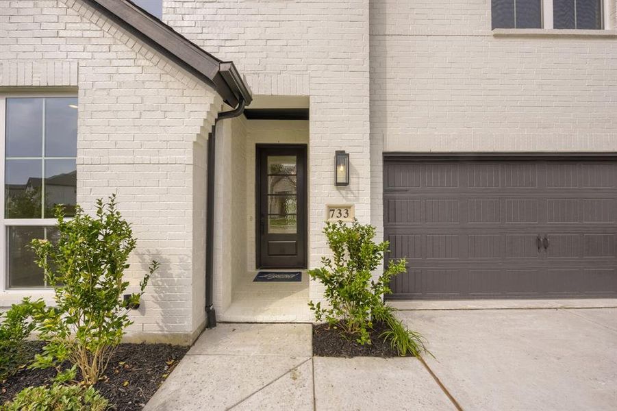 White brick exterior featuring a dark paneled entry door with glass inserts, a single exterior sconce, and an attached garage with a dark sectional door