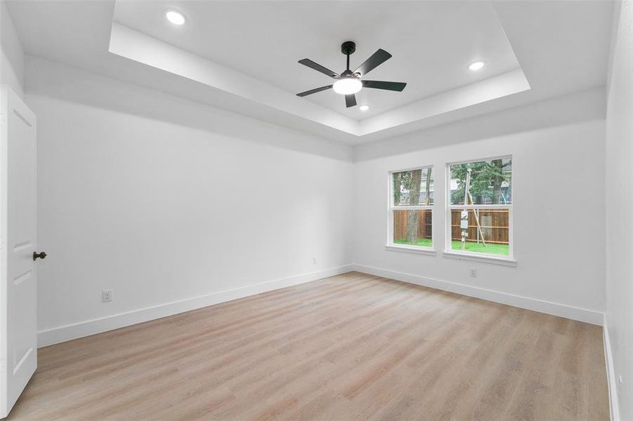 Spacious room featuring a tray ceiling with recessed lighting, a ceiling fan, two windows, and wood-finish flooring Spacious room featuring a tray ceiling with recessed lighting, a ceiling fan, two windows, and wood-finish flooring