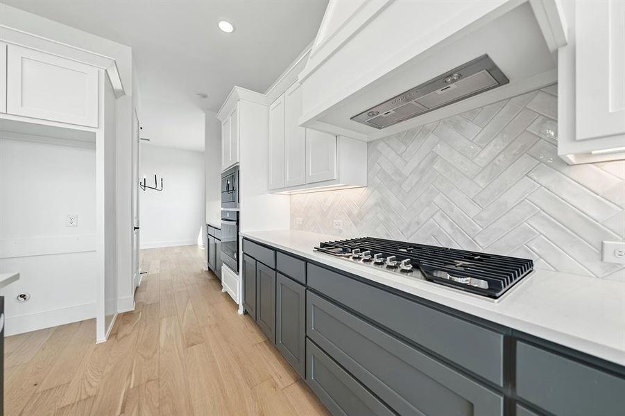 Kitchen featuring white cabinetry, extractor fan, light wood-type flooring, gray cabinetry, and appliances with stainless steel finishes