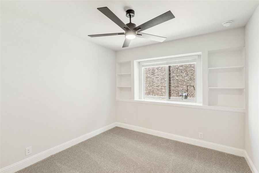 Empty bedroom with built-in shelves flanking a window, ceiling fan, and neutral carpet Empty bedroom with built-in shelves flanking a window, ceiling fan, and neutral carpet
