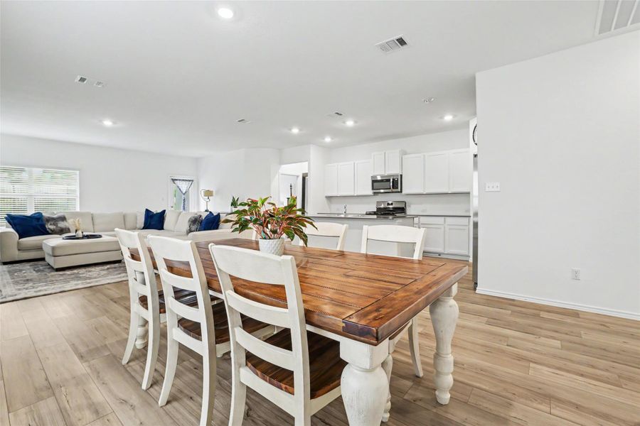 Open-concept living space featuring wood-finish flooring, recessed lighting, and a kitchen with white cabinetry and stainless steel appliances