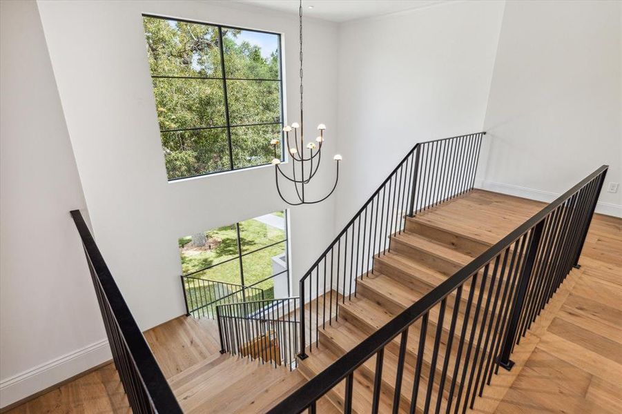 This wide, luxurious staircase elegantly ascends to the second floor, serving as one of two stunning staircases in the home. Illuminated by a Kelly Wearstler alabaster chandelier, the two-story window offers a captivating glimpse of the interior from the street, showcasing the home's exquisite design.