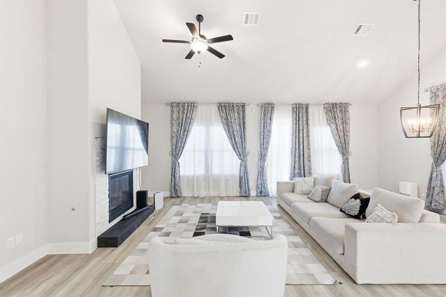 Living room featuring a glass covered fireplace, light wood finished floors, a ceiling fan, a chandelier, and high vaulted ceiling
