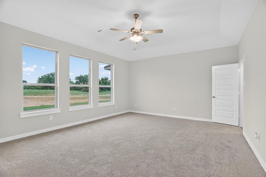 Spacious room featuring three large windows, neutral-toned carpeting, light gray walls, a contemporary ceiling fan, and a paneled white door