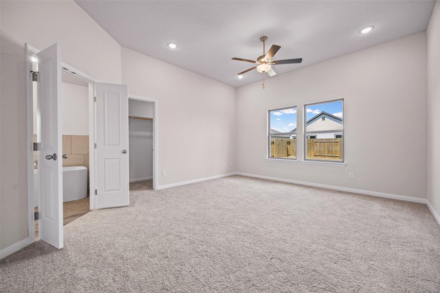 A spacious primary bedroom features neutral-toned carpeting, high ceilings, and access to an en-suite bath. A spacious primary bedroom features neutral-toned carpeting, high ceilings, and access to an en-suite bath.