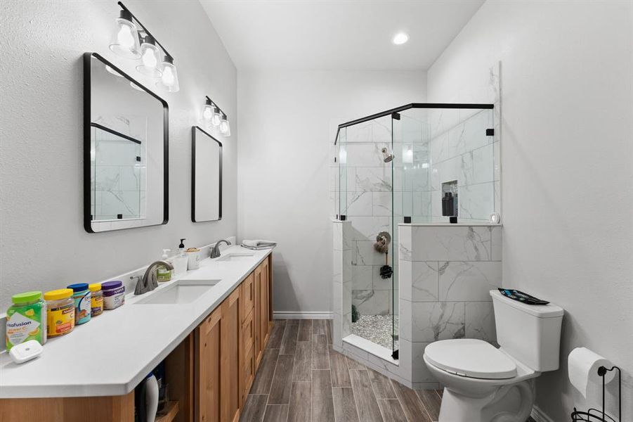 Master bathroom with tile, walk in shower, soap nook, quartz countertops, dual vanity with decorative mirrors and shelving for storage.