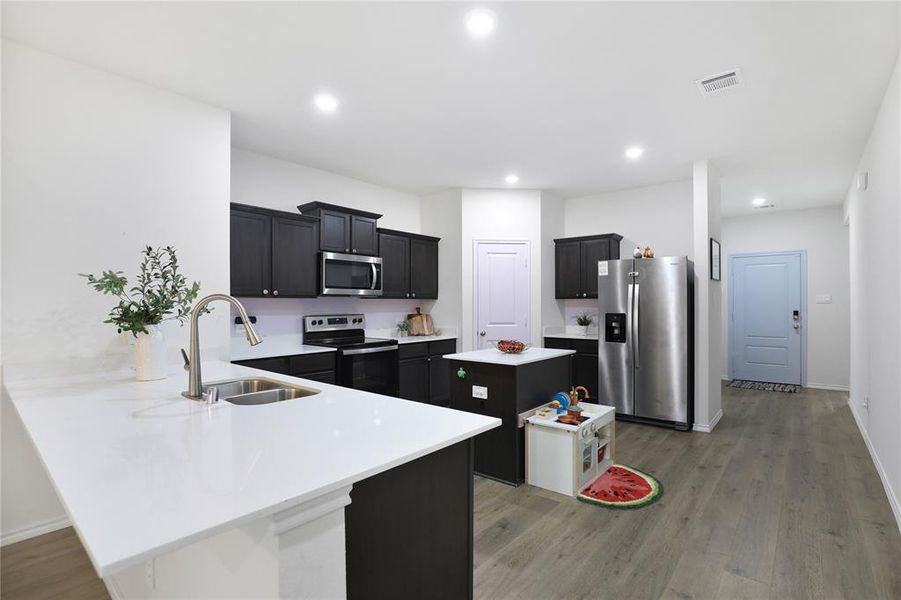 Kitchen featuring a center island, dark cabinetry, light wood-style flooring, appliances with stainless steel finishes, and recessed lighting