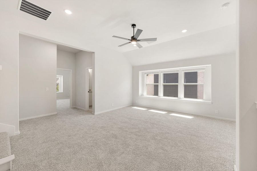Spacious empty bedroom with vaulted ceiling, ceiling fan, carpet flooring, and large windows