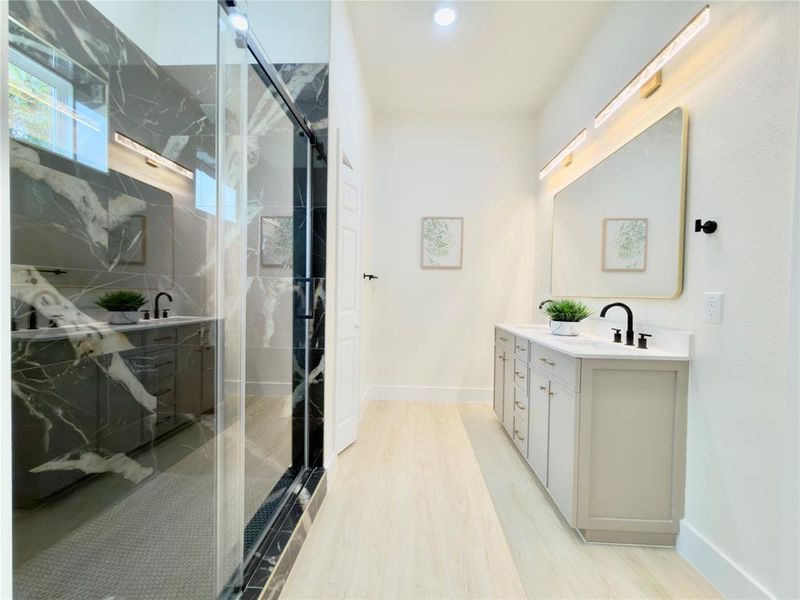 Bathroom featuring a marble finish shower, double vanity, light wood-style floors, and recessed lighting