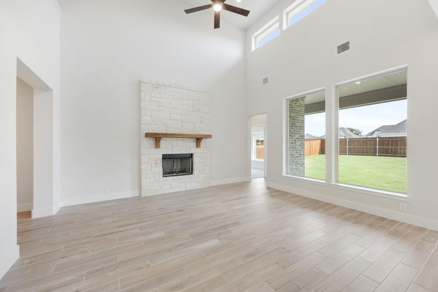 Open living room with vaulted ceiling, stone fireplace, wood mantel, and large windows overlooking backyard