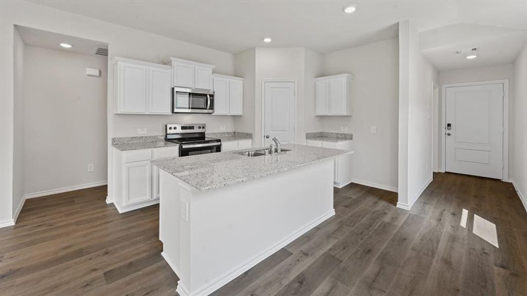 Kitchen featuring a central island with an undermount sink, granite countertops, white cabinetry, stainless steel appliances, and wood-finish flooring