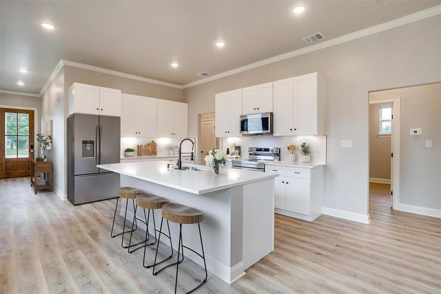 Kitchen featuring a sink, appliances with stainless steel finishes, a kitchen breakfast bar, and light wood-style floors Kitchen featuring a sink, appliances with stainless steel finishes, a kitchen breakfast bar, and light wood-style floors