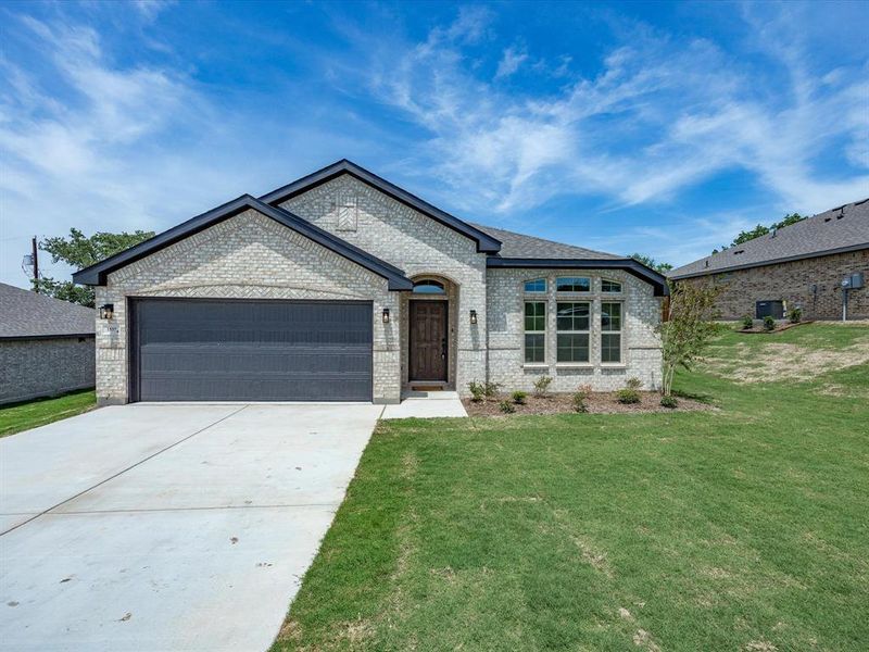 Single-story residence featuring light-colored brick exterior, dark grey garage door, archway entry, and multiple front windows Single-story residence featuring light-colored brick exterior, dark grey garage door, archway entry, and multiple front windows