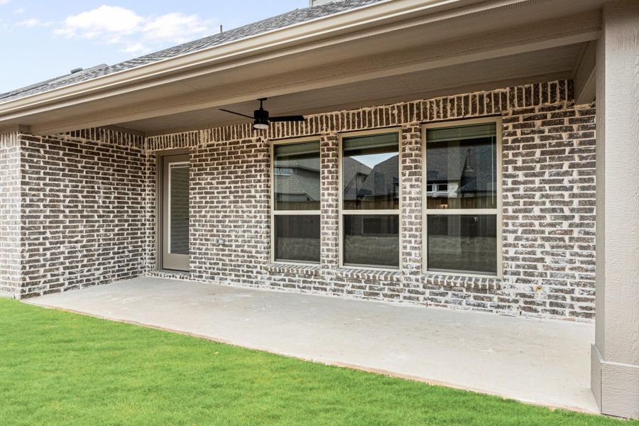 Covered back patio with ceiling fan, brick exterior, large windows, and concrete slab overlooking green lawn Covered back patio with ceiling fan, brick exterior, large windows, and concrete slab overlooking green lawn