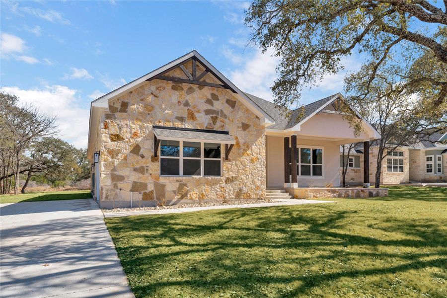 View of front of property with a front yard, stone siding, and covered porch