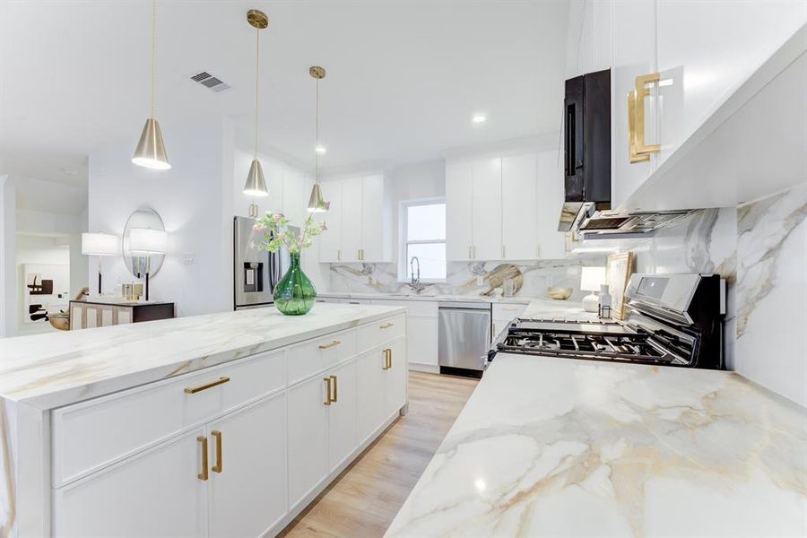 This stunning kitchen features gold hardware, quartz countertops, gas range, and stainless steel appliances. There is plenty of storage space in the cabinets.