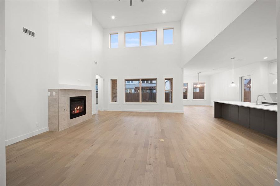Unfurnished living room with light wood-style flooring, a fireplace, plenty of natural light, recessed lighting, and a high ceiling