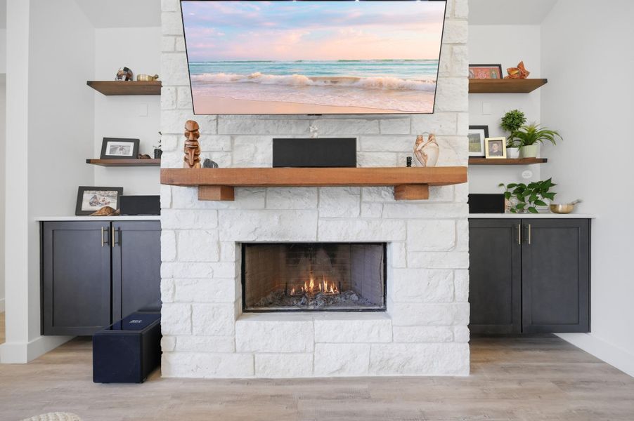 A stone fireplace anchors the room, flanked by custom built-in cabinetry and open wood shelving.