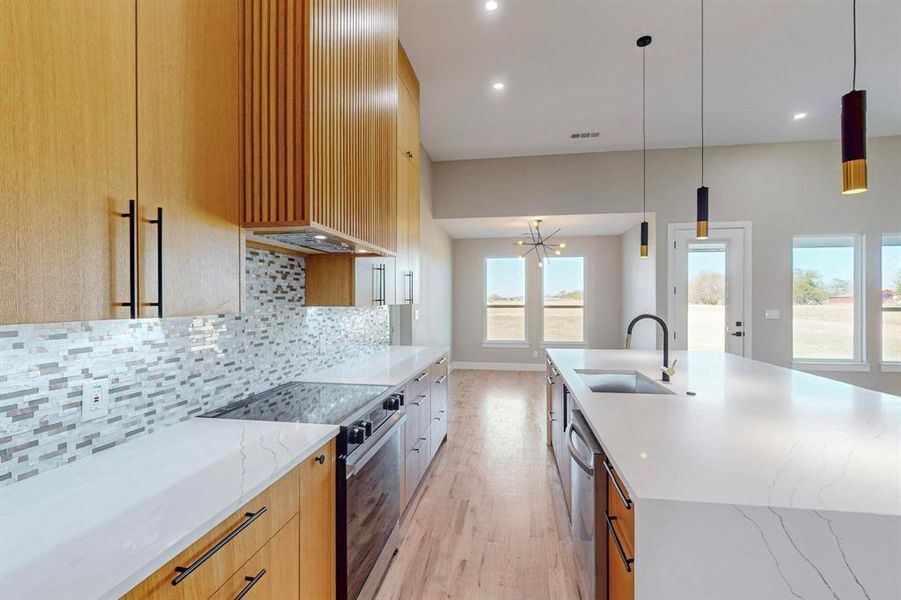 Kitchen with light stone countertops, sink, appliances with stainless steel finishes, and pendant lighting