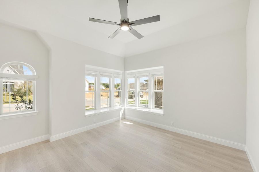 Empty room with light wood floors, ceiling fan, and large corner windows with arched accent window