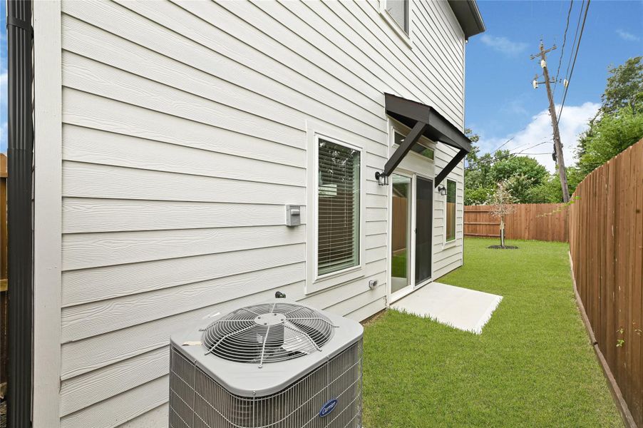This photo shows a side view of a house with light-colored siding, featuring a small backyard space with a neatly maintained lawn. There are two large windows and a sliding glass door leading to the yard, with a wooden fence providing privacy. An air conditioning unit is visible next to the house. This photo shows a side view of a house with light-colored siding, featuring a small backyard space with a neatly maintained lawn. There are two large windows and a sliding glass door leading to the yard, with a wooden fence providing privacy. An air conditioning unit is visible next to the house.