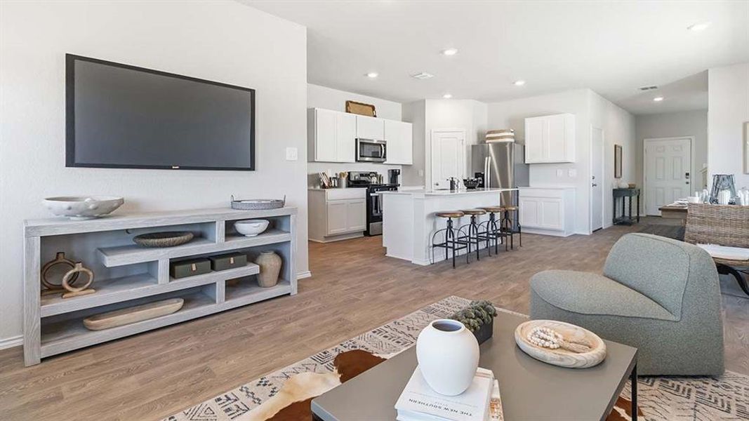 Open-concept living space featuring wood-finish flooring, recessed lighting, a kitchen island with seating, white cabinetry, and stainless steel appliances