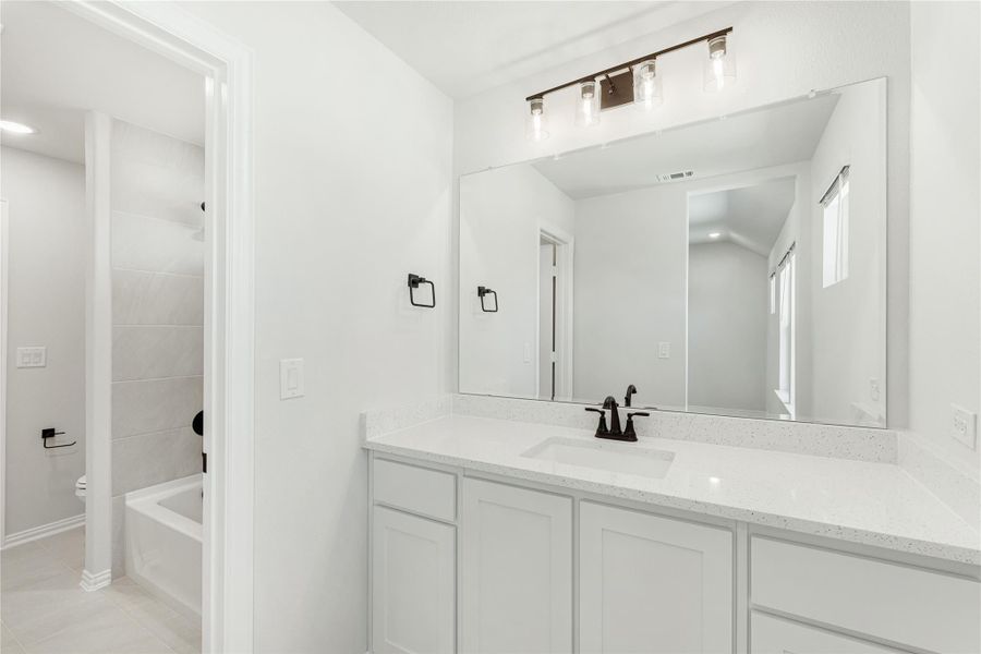 Bathroom with white vanity, quartz countertop, large mirror, and separate tub and shower area visible through doorway.